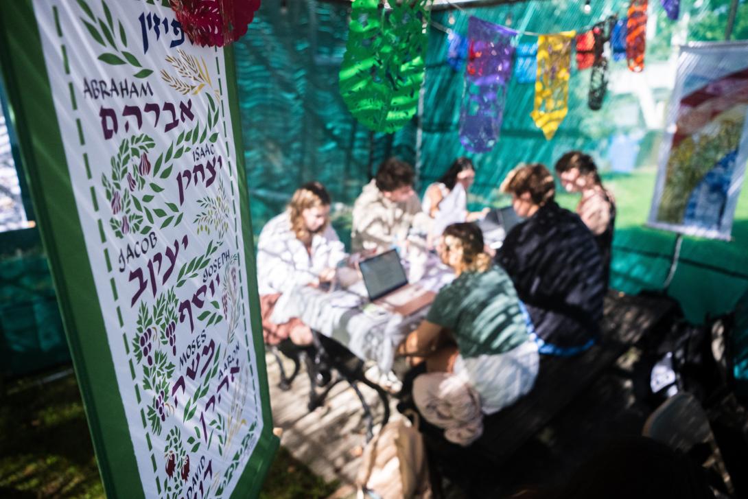 A banner shows words written in hebrew and english with students sitting at a table in the background