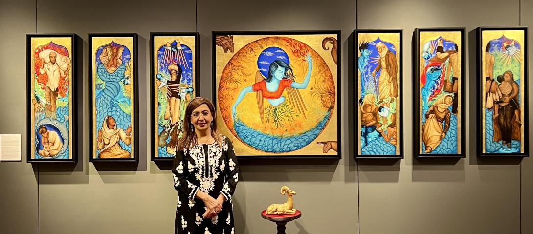 Siona Benjamin stands in front of her painting Exodus. There are 7 canvases painted with Jewish symbolism in bright colors